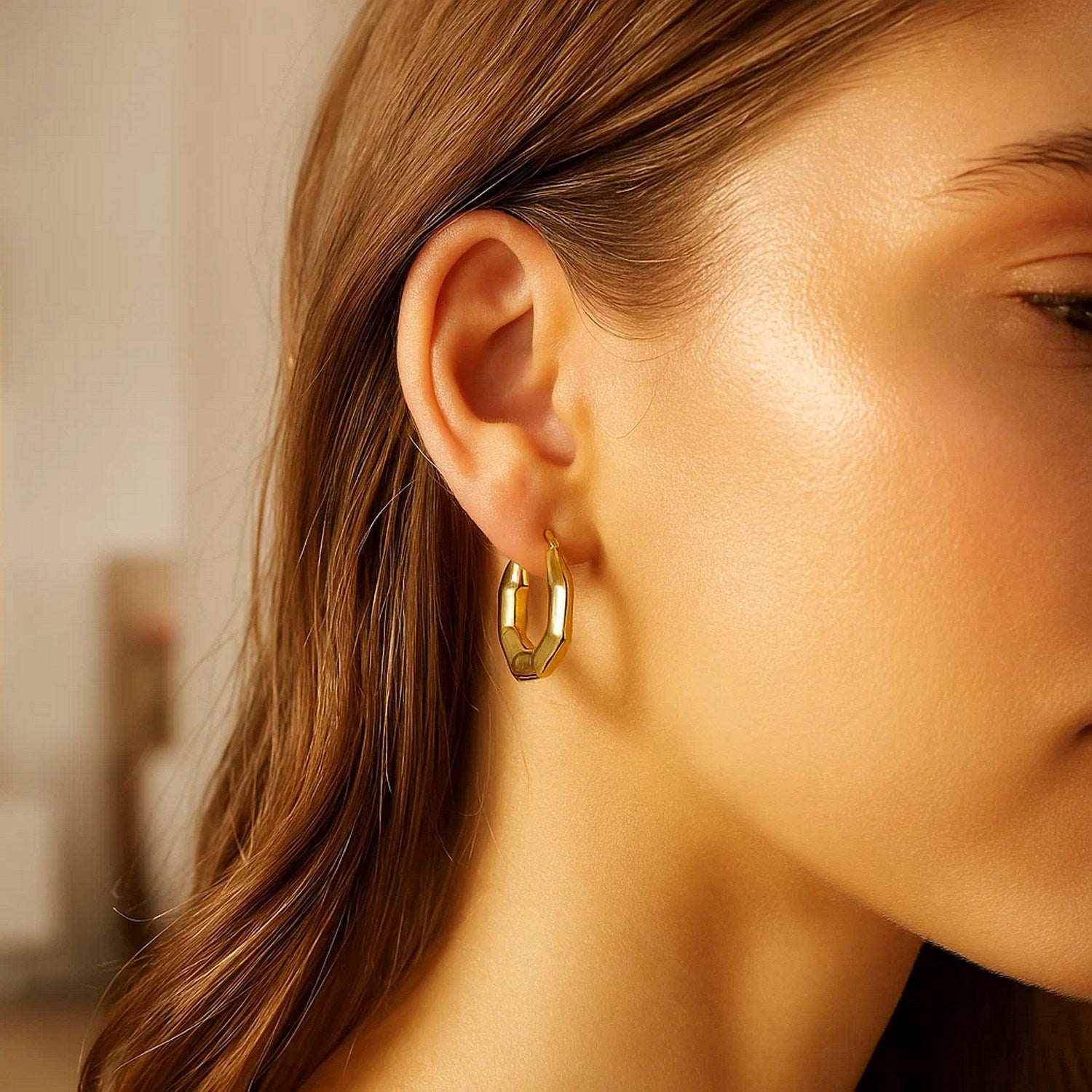 14k yellow gold octagon hoop earrings on a woman's ear.