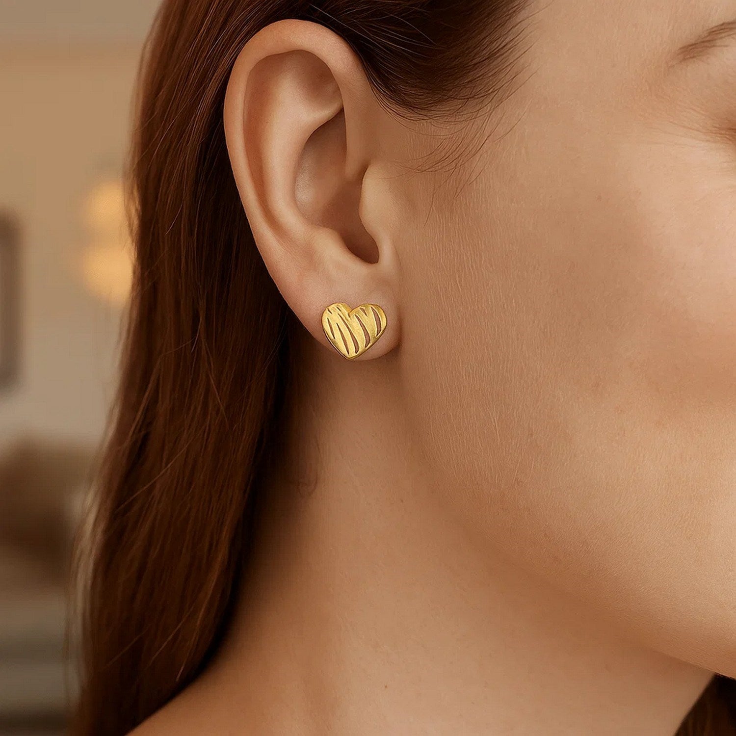 A woman wears a single 14K yellow gold scribble heart stud earring.
