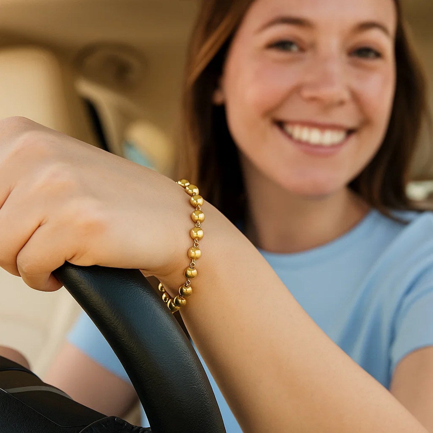 14K yellow gold polished pebble bead bracelet on a woman's wrist while driving.
