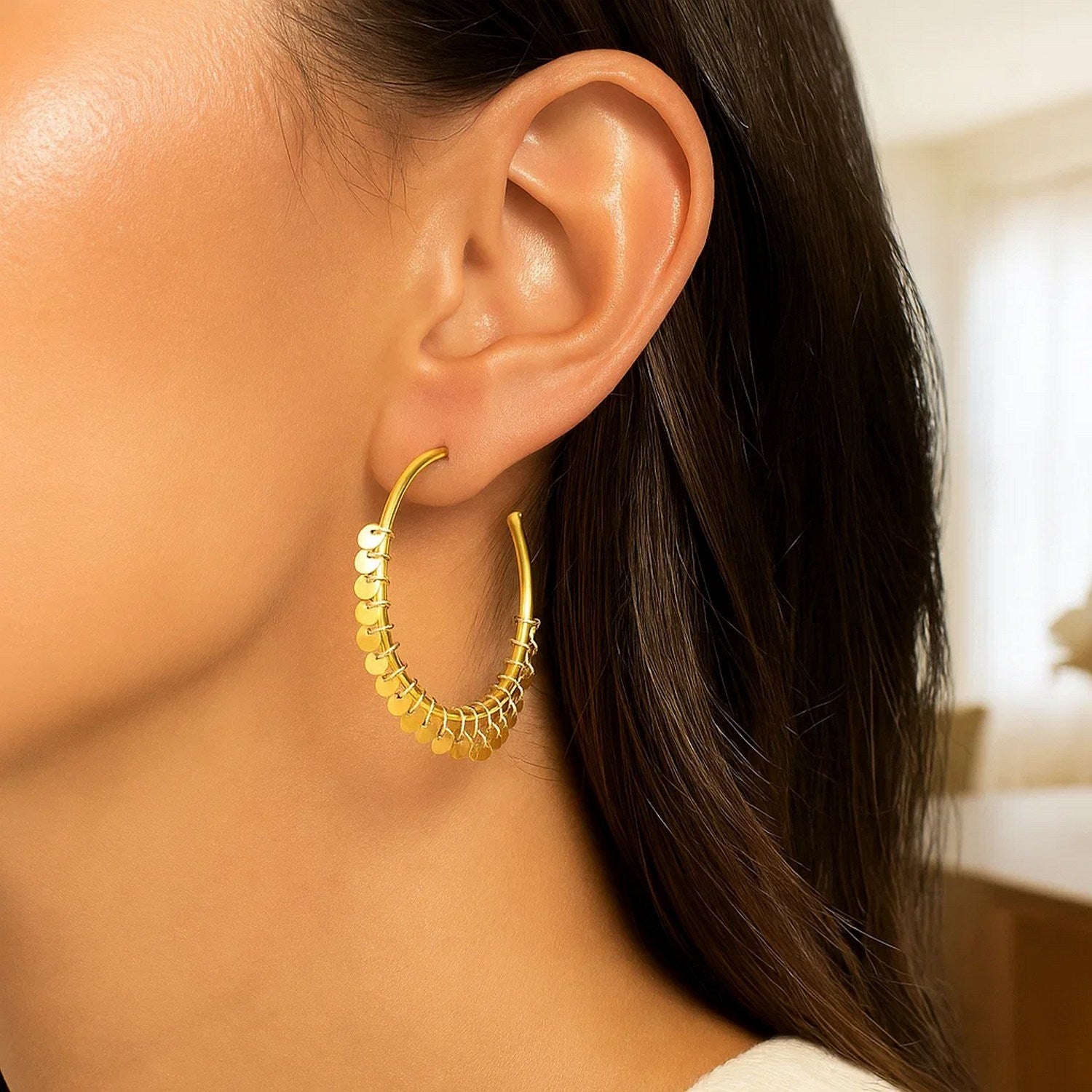 14k yellow gold hoop earrings with dangling sequins on a woman's ear.