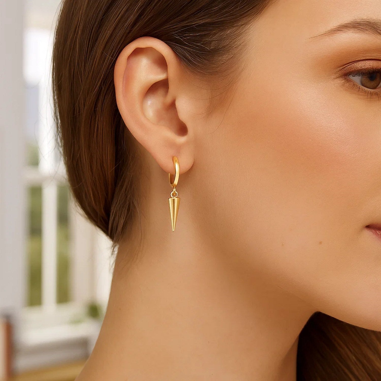 A woman wears a single 14K yellow gold dangling spike drop hoop earring.