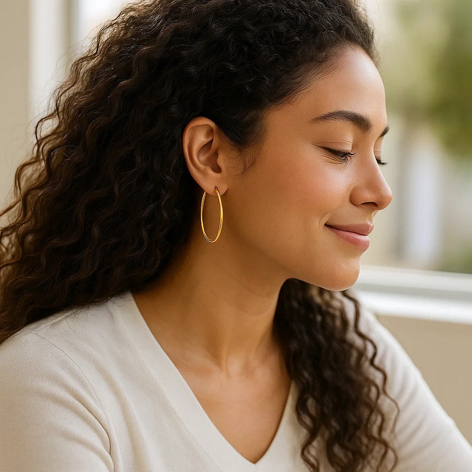 14k yellow gold slim oval hoop earrings on a woman with curly hair.