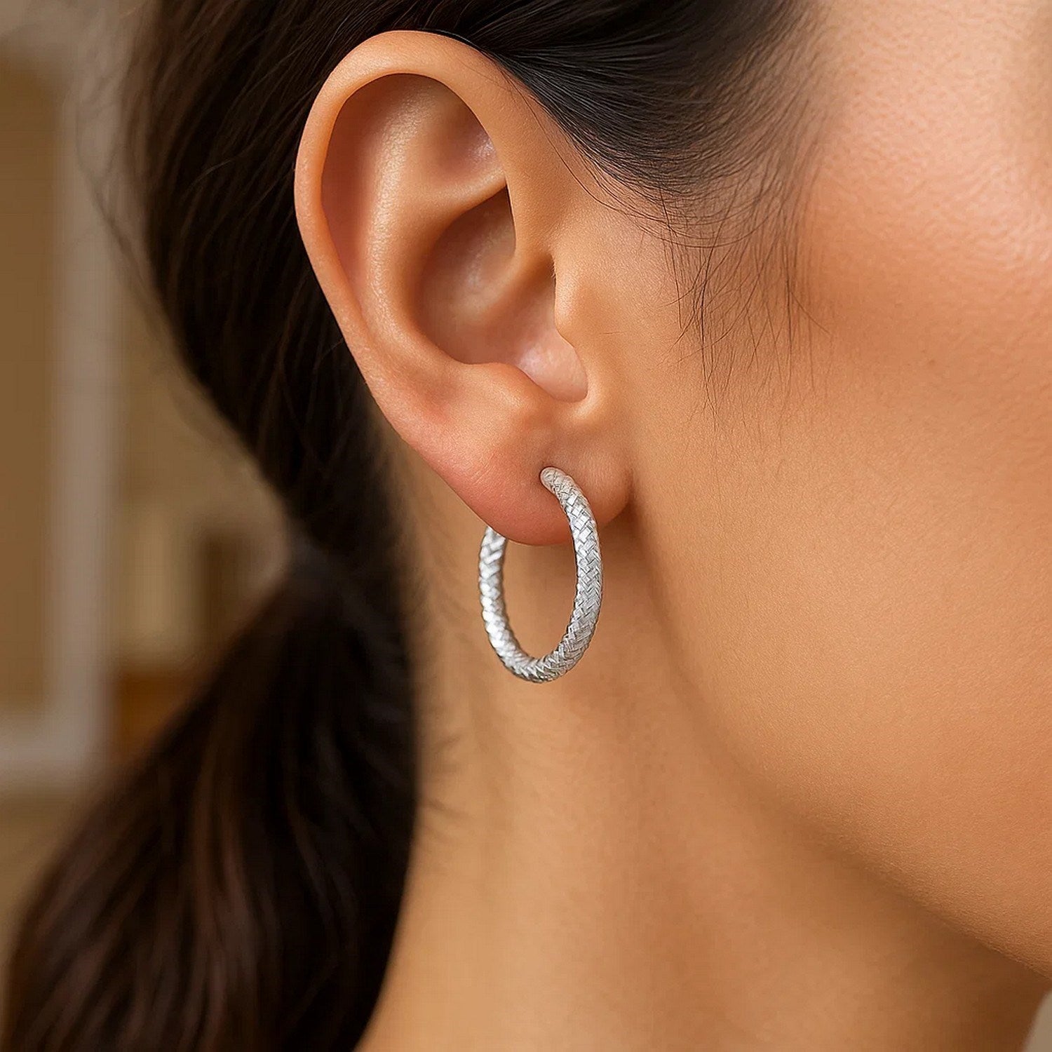 Sterling silver large hoop earrings with a braid texture are worn on an ear.