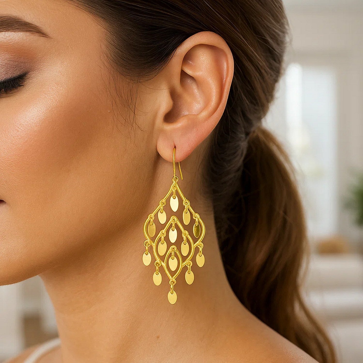 14K yellow gold polished chandelier earrings with open oval shapes on a woman's ear.