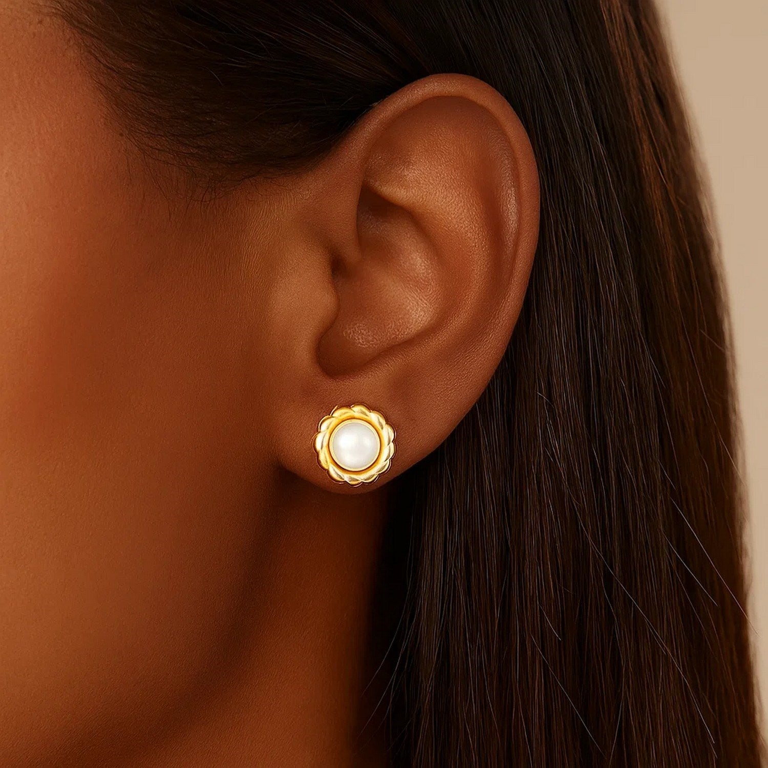 A single 14k yellow gold flower stud earring with a pearl is worn on an ear.