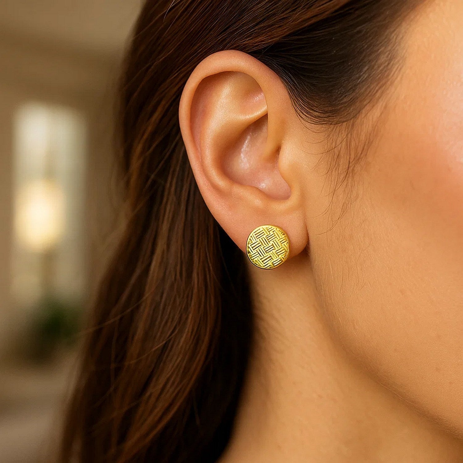 14k yellow gold post earrings with textured circles on a woman's ear.