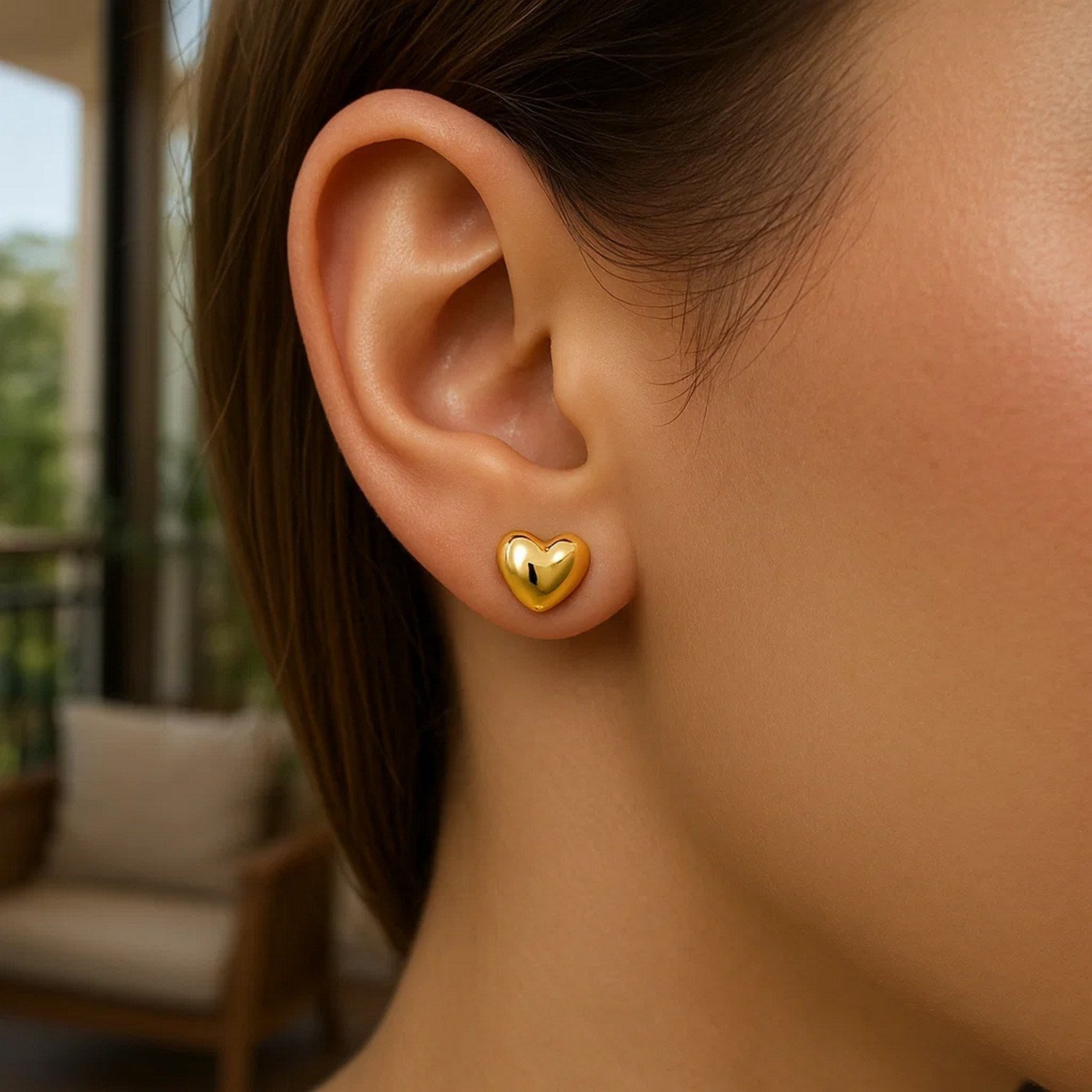 14k yellow gold puffed heart shape shiny earrings on a woman's ear.