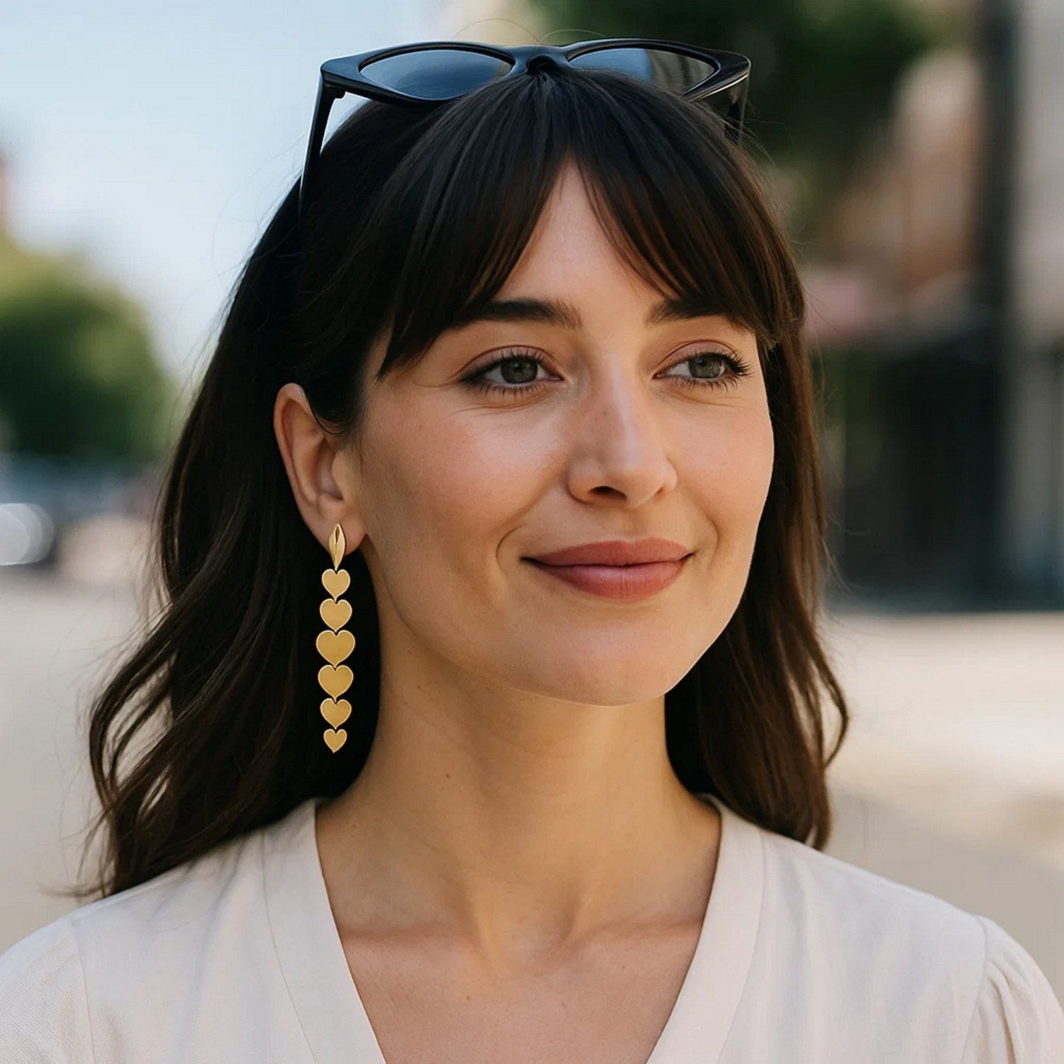 14K yellow gold heart drop earrings on a woman with dark hair and sunglasses.