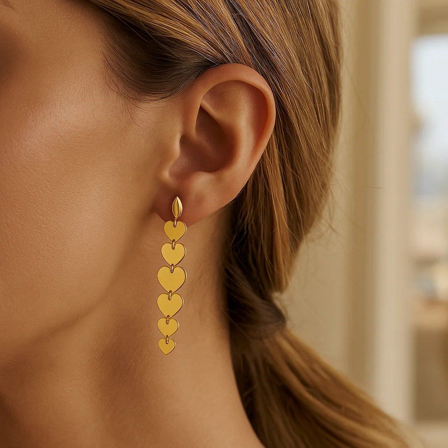 14K yellow gold heart drop earrings are shown on a woman's ear.