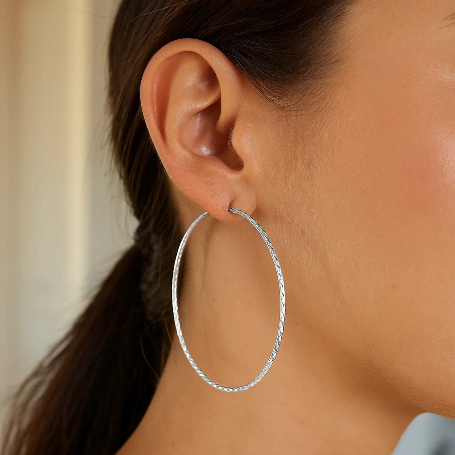 Sterling silver large textured round hoop earrings are worn on a woman's ear.