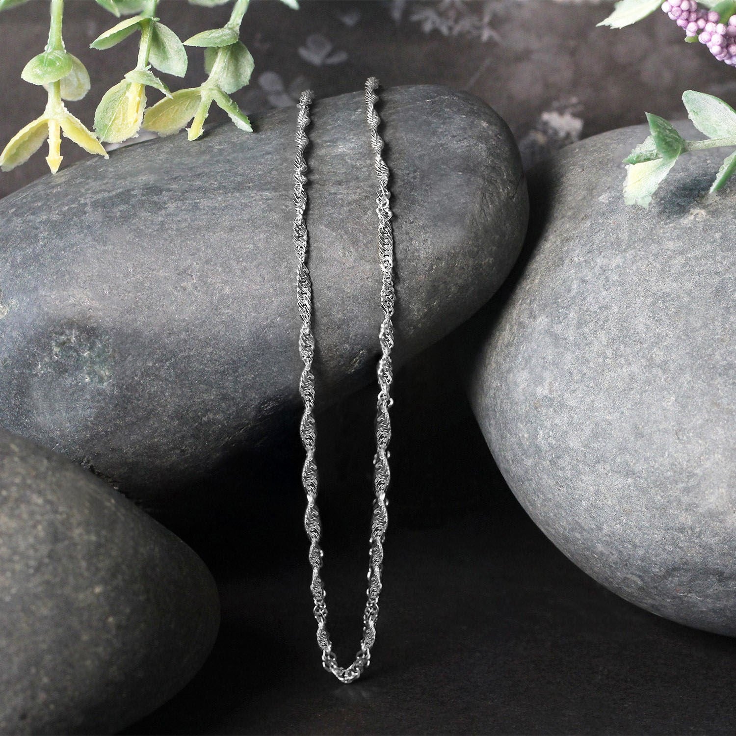 A 14k white gold Singapore chain is draped over dark grey stones.