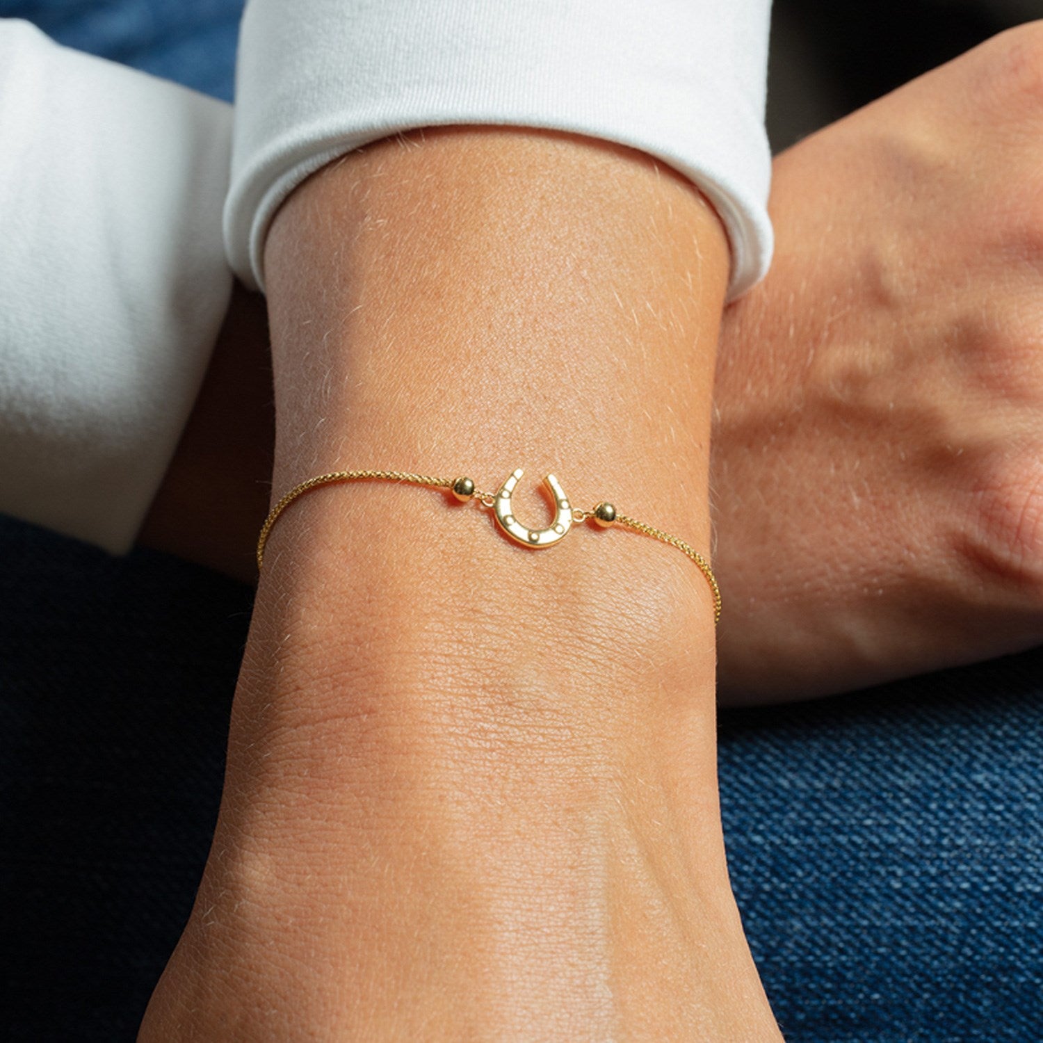 Adjustable 14K yellow gold bracelet with a horseshoe charm and two small beads.