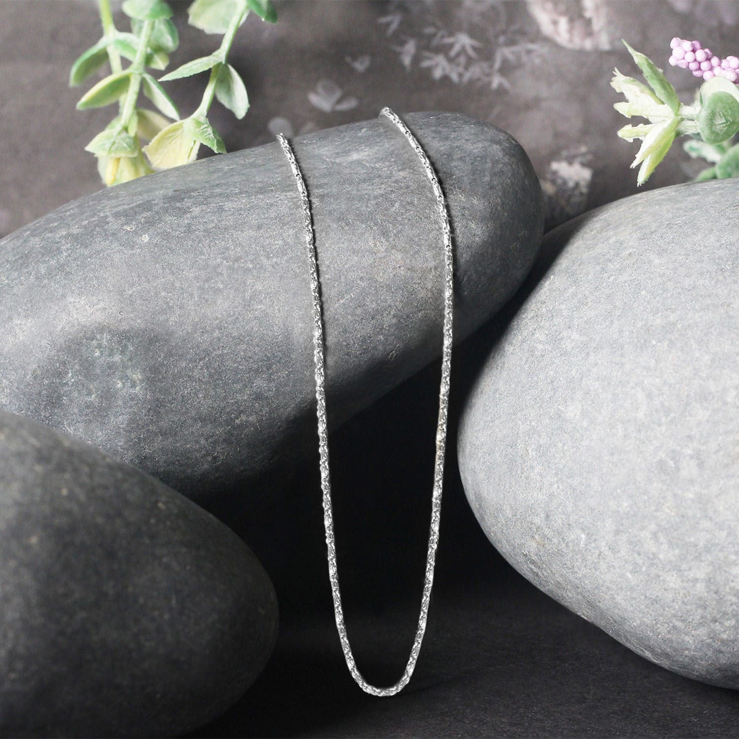 14k white gold Lumina pendant chain draped over smooth gray stones.