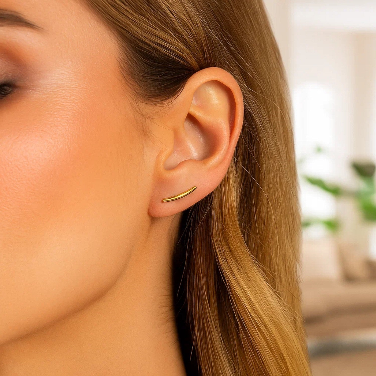 14k yellow gold curve climber post earrings on a woman's ear.