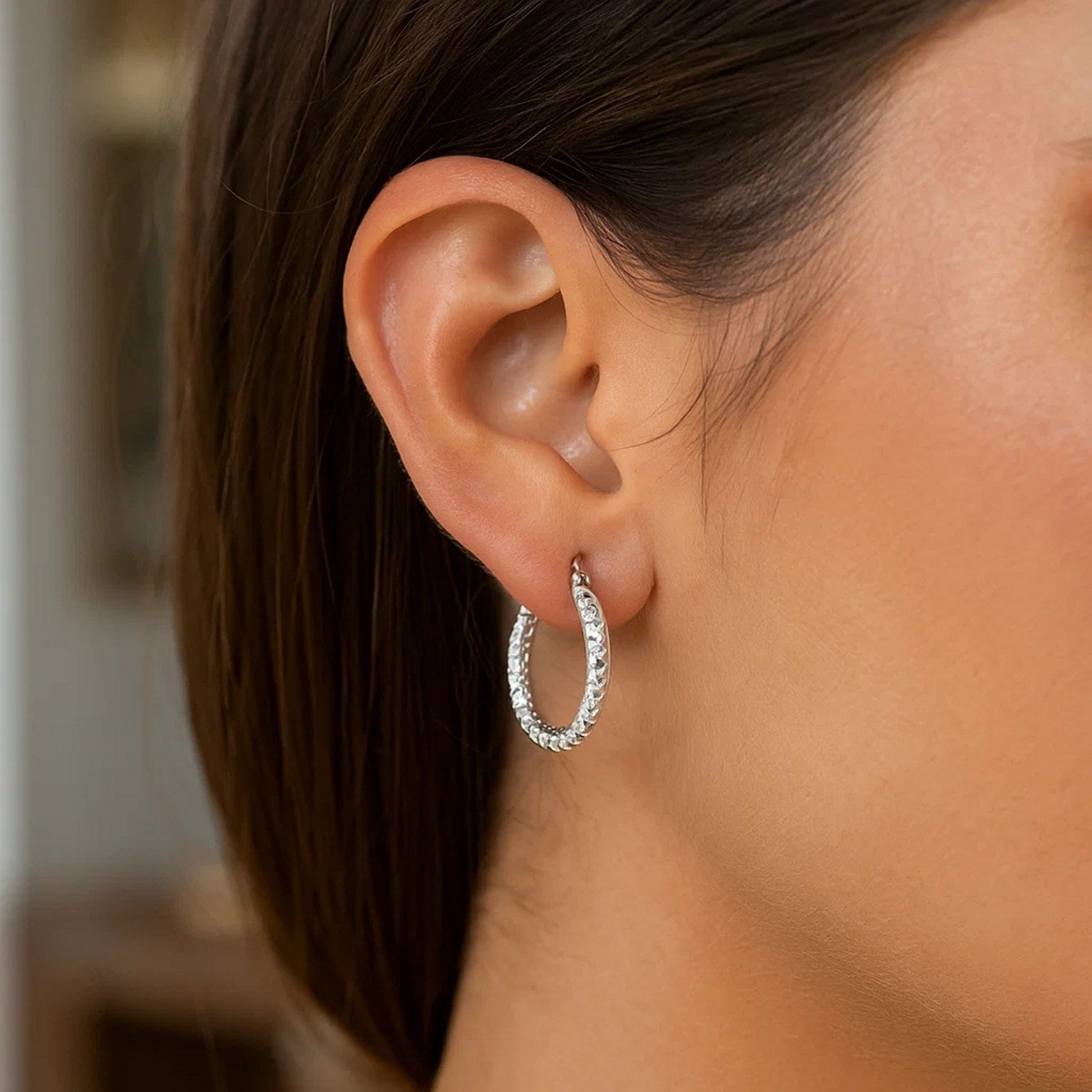A woman wears a sterling silver faceted hoop earring with rhodium finishing.