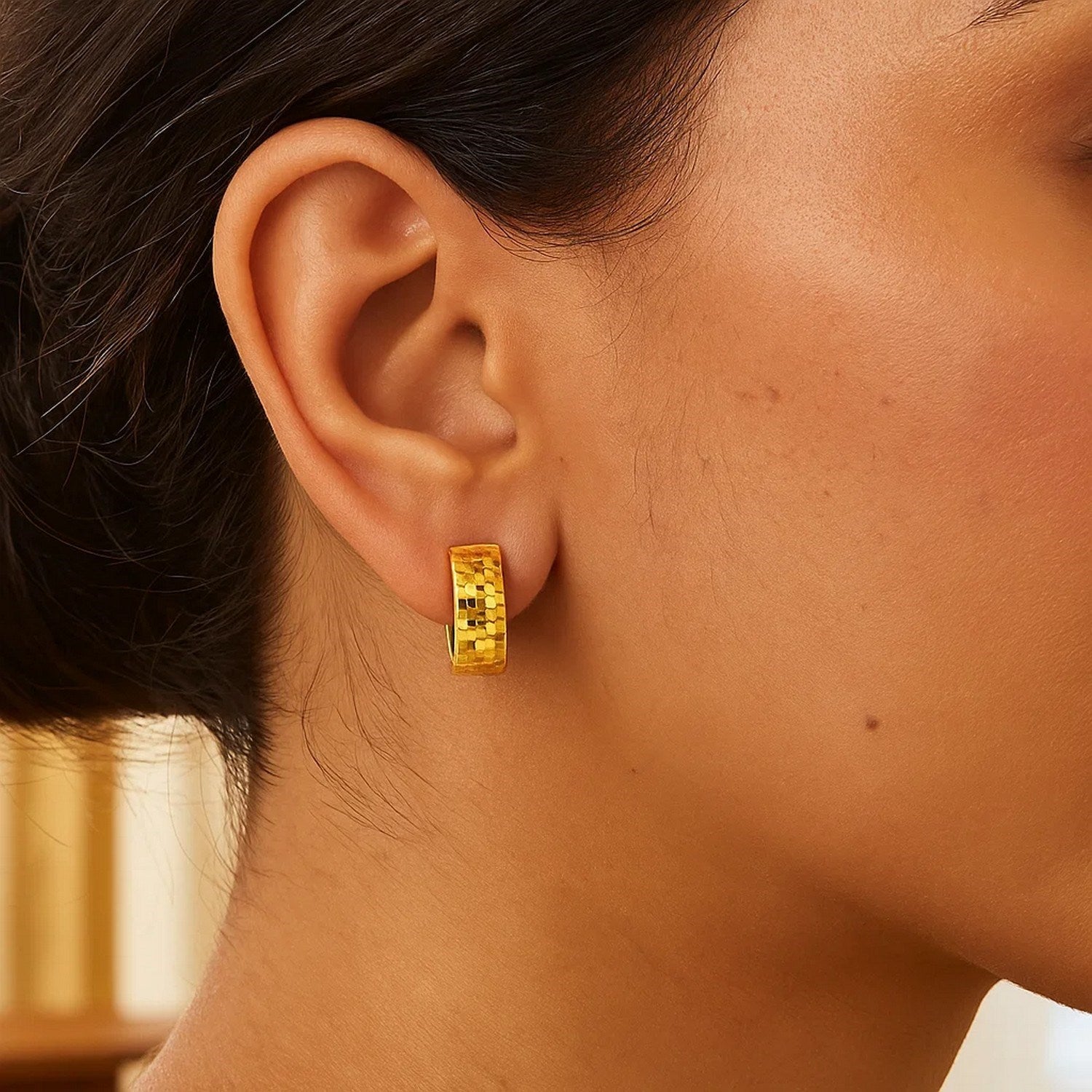 14k yellow gold textured and polished hoop earrings on a model's ear.