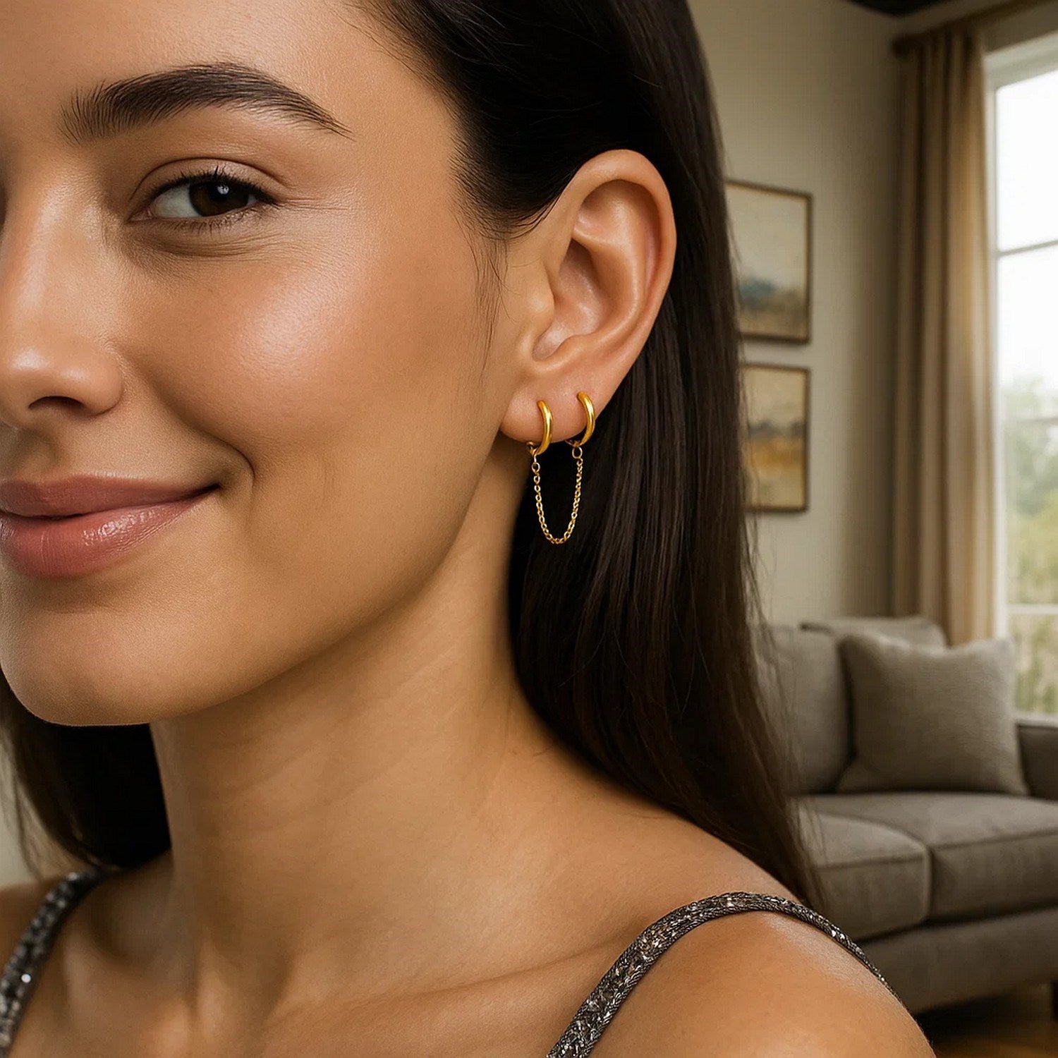 14k yellow gold two-hole huggie style hoop earrings with a delicate chain on a model.