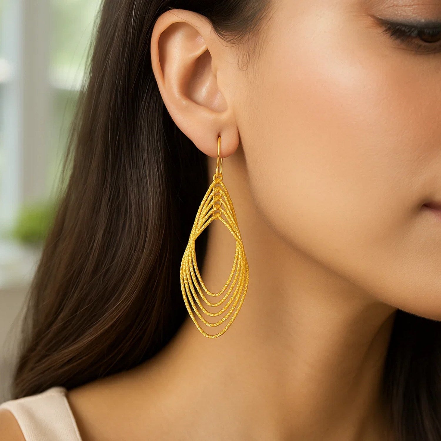 14k yellow gold post earrings with textured marquise shapes on a woman's ear.