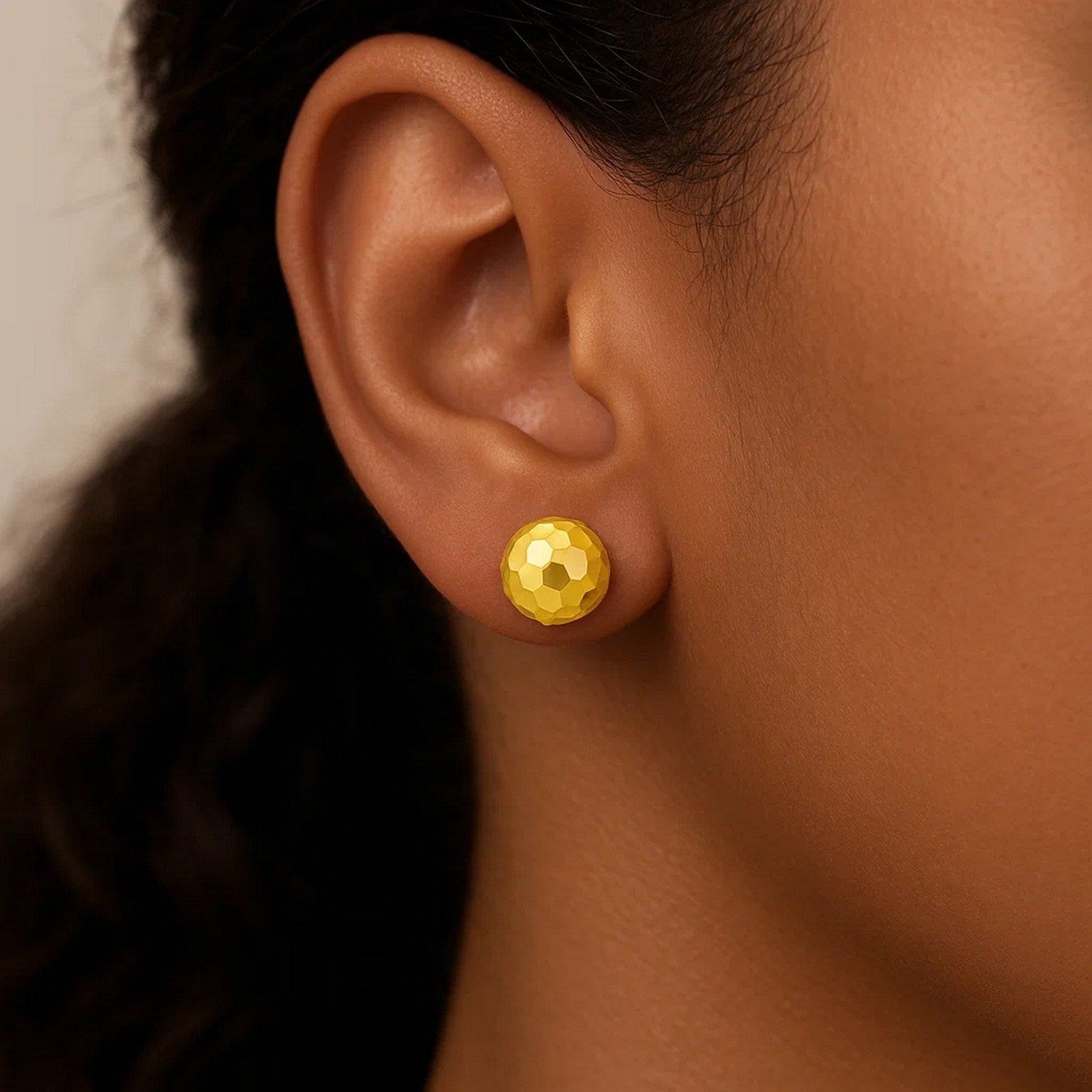 14k yellow gold round faceted stud earrings on an ear.