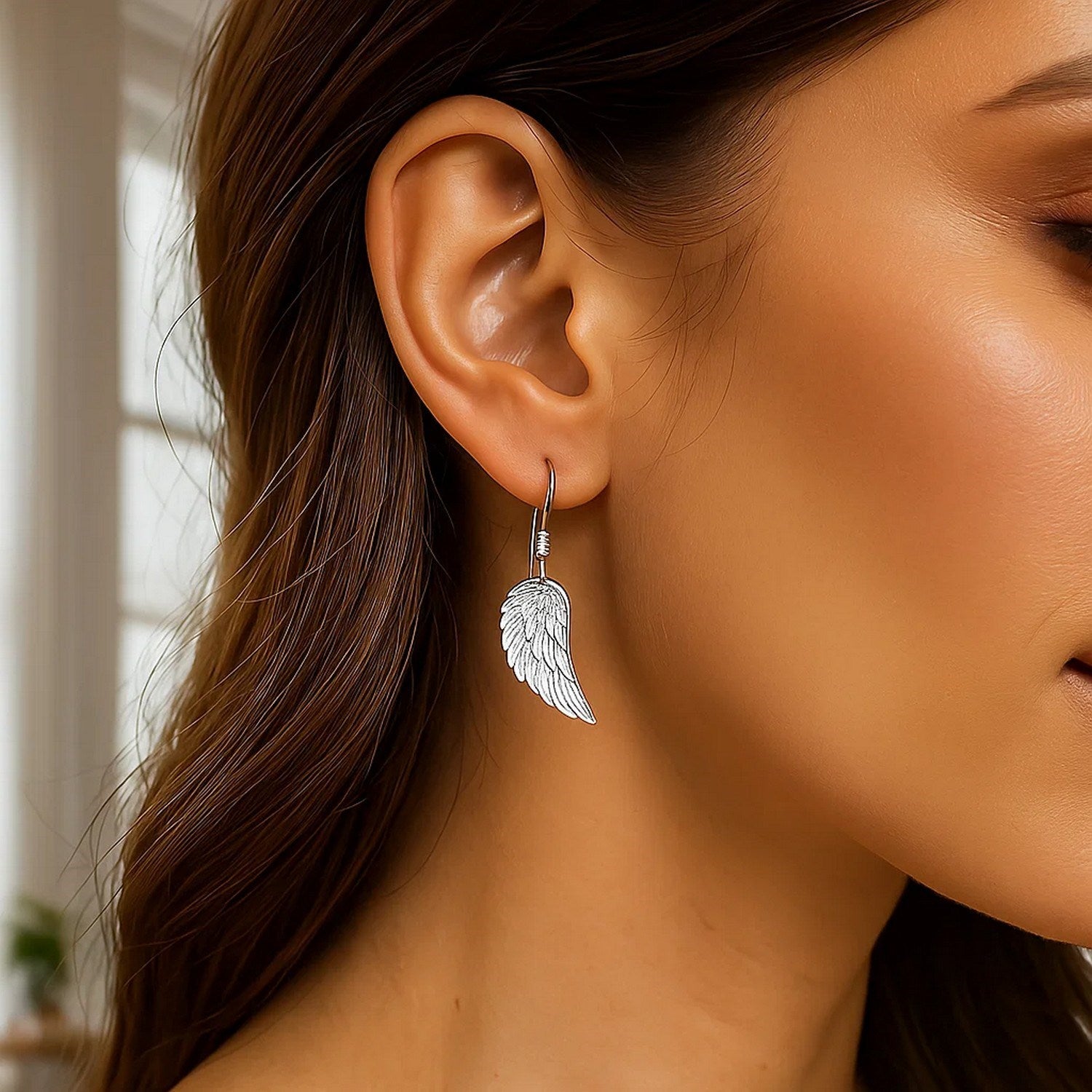 Sterling silver textured angel wing earrings hang from a woman's ear.