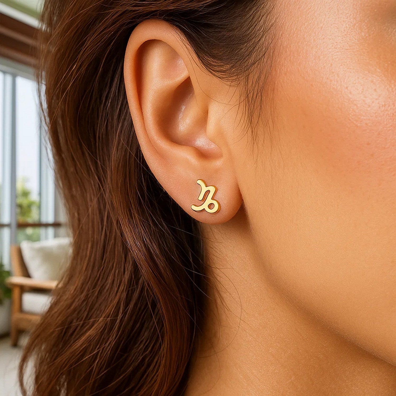 A woman wears a single 14k yellow gold Capricorn stud earring.