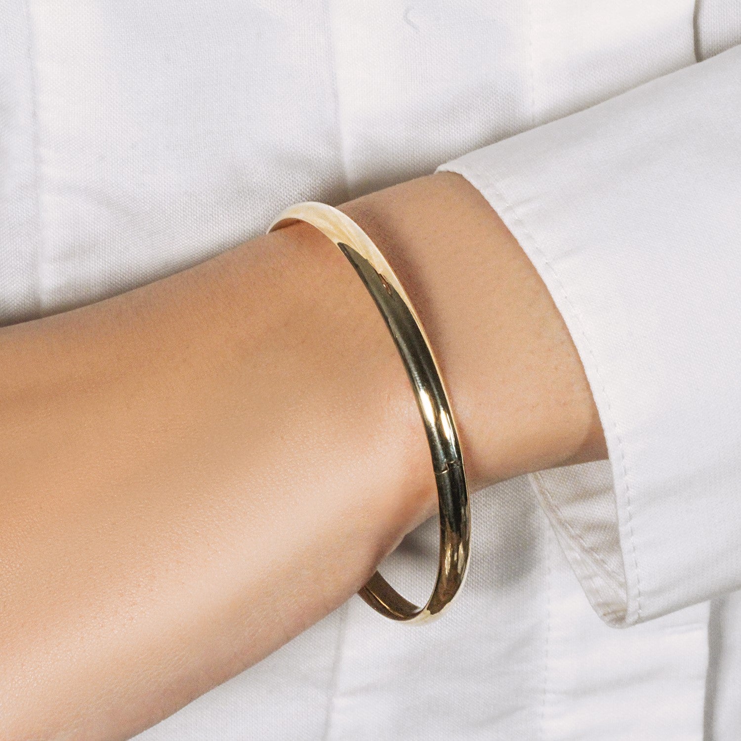 A shiny 10k yellow gold dome style bangle on a person's arm.