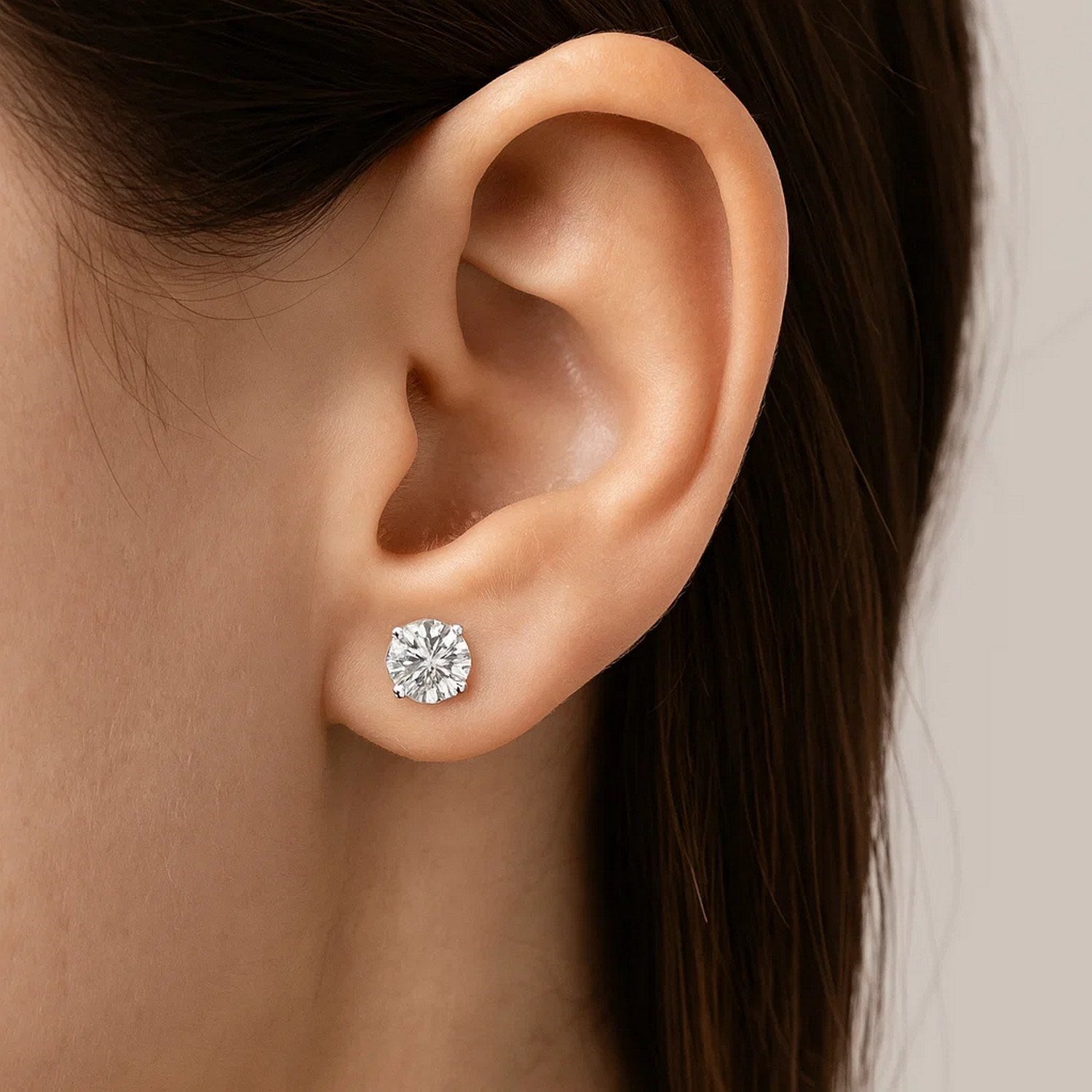A single round, faceted cubic zirconia stud earring in sterling silver on an ear.