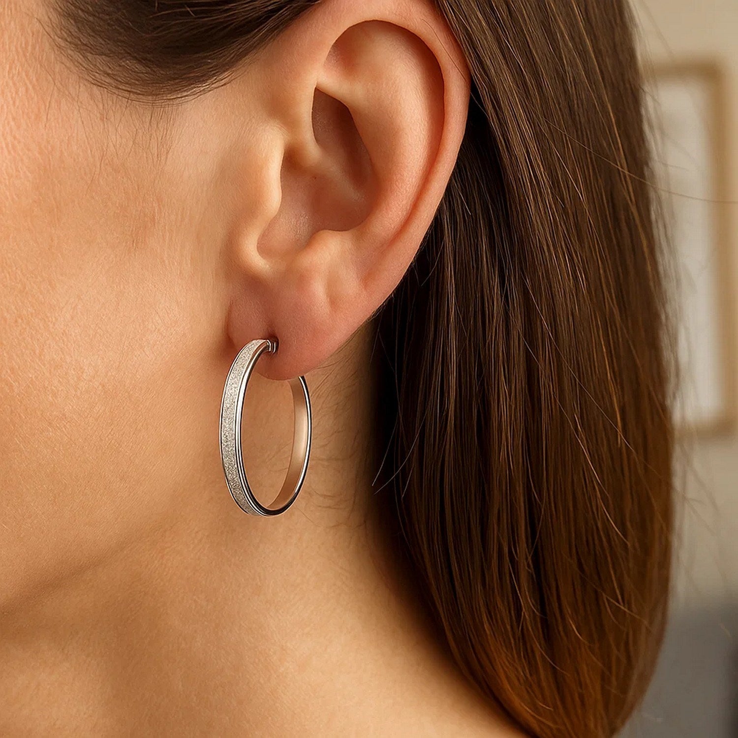 A woman wears a single white tone gold hoop earring with a glitter-look design.