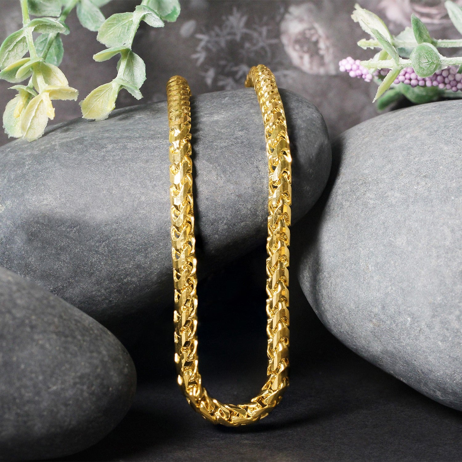 A 14k yellow gold diamond-cut round Franco chain is draped over gray rocks.