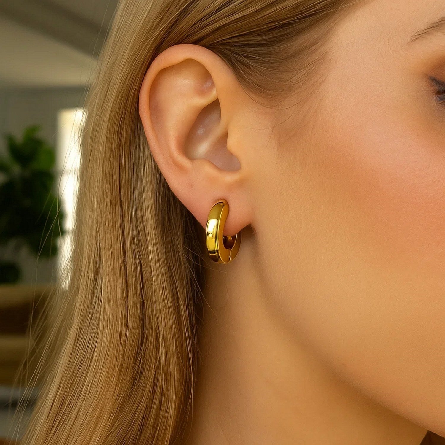 14K yellow gold thick post hoop earring on a woman's ear.