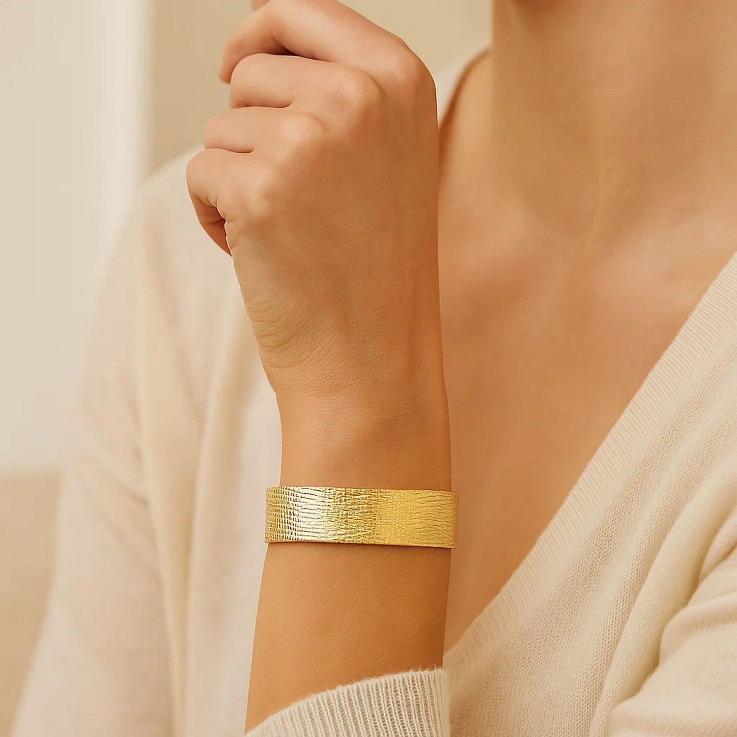 A woman wears a wide, textured 14K yellow gold bracelet on her left wrist.