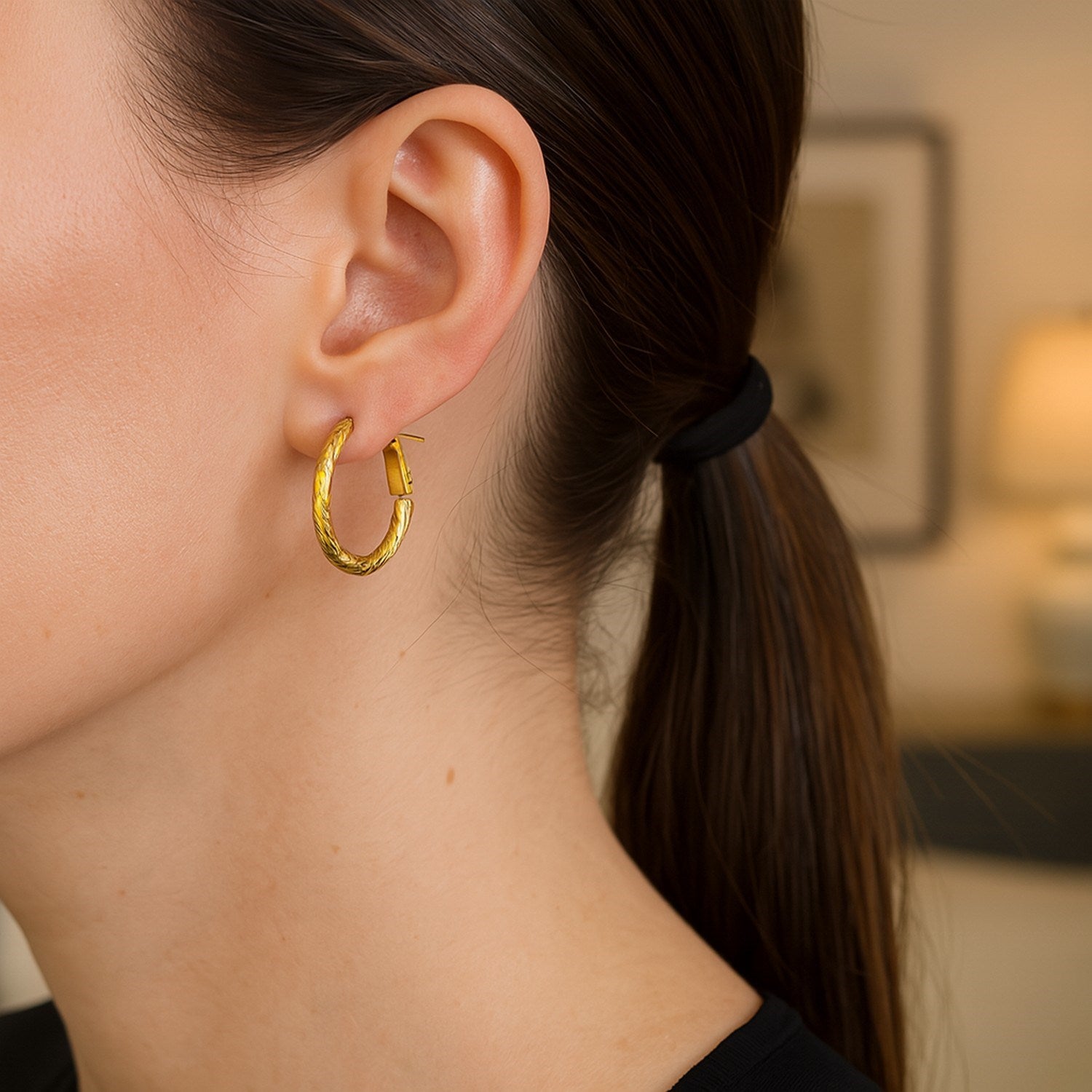 A woman wears a single 14k yellow gold petite twisted round hoop earring.