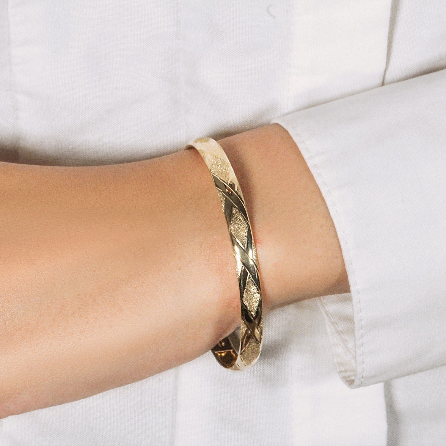 10k yellow gold slender bangle with a diamond pattern and textured finish on a person's wrist.
