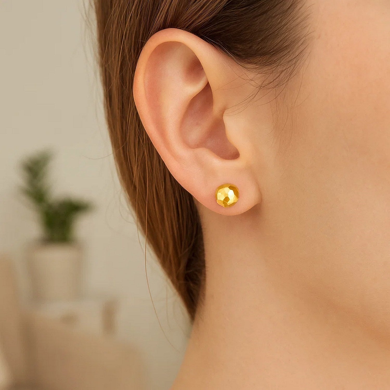 A single 14k yellow gold faceted ball earring is worn on an ear.