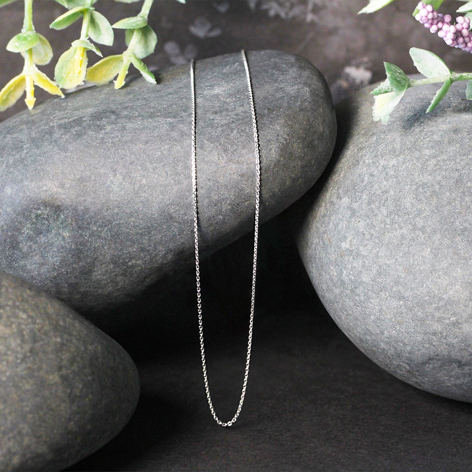 A delicate 14k white gold cable link chain draped over smooth grey stones.
