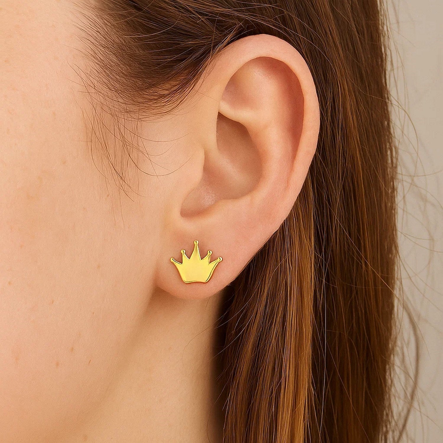 14k yellow gold crown post earrings are worn on an ear.